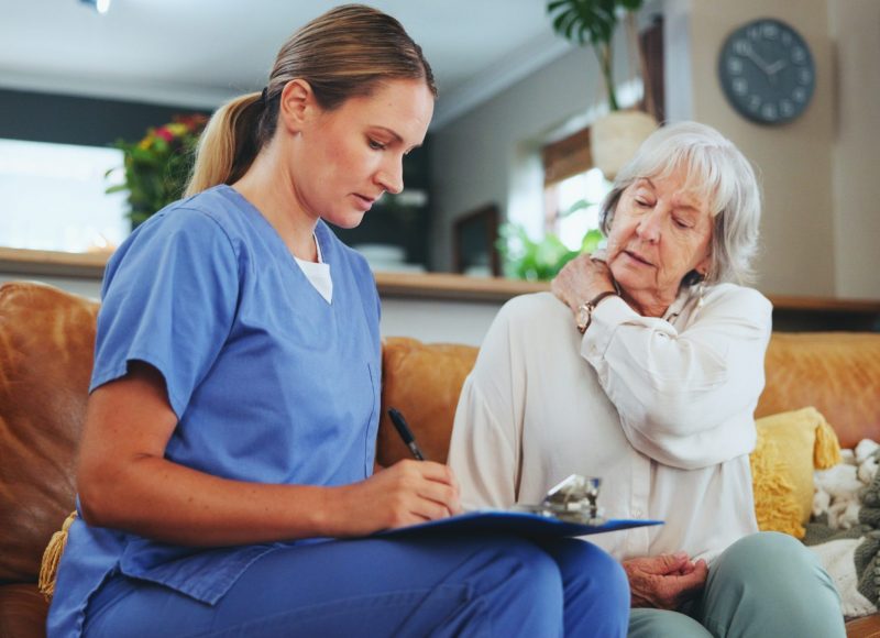 Senior woman, nurse and writing with consultation for elderly care, pain or injury at old age home