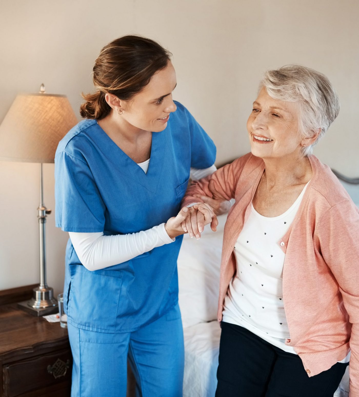 Shot of a young nurse helping a senior woman get up from her bed in a nursing home.